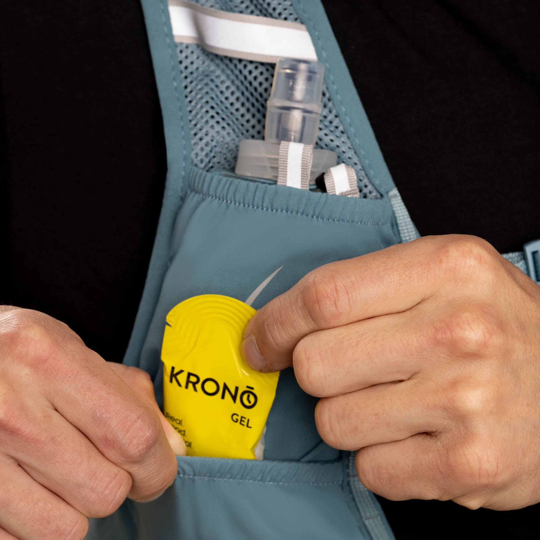 Person holding a blue waist bag with a yellow 'KRONÓ' gel pack. #color_steel-blue