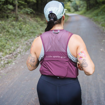 Person running on a trail wearing a purple sports vest with visible branding. #color_plume