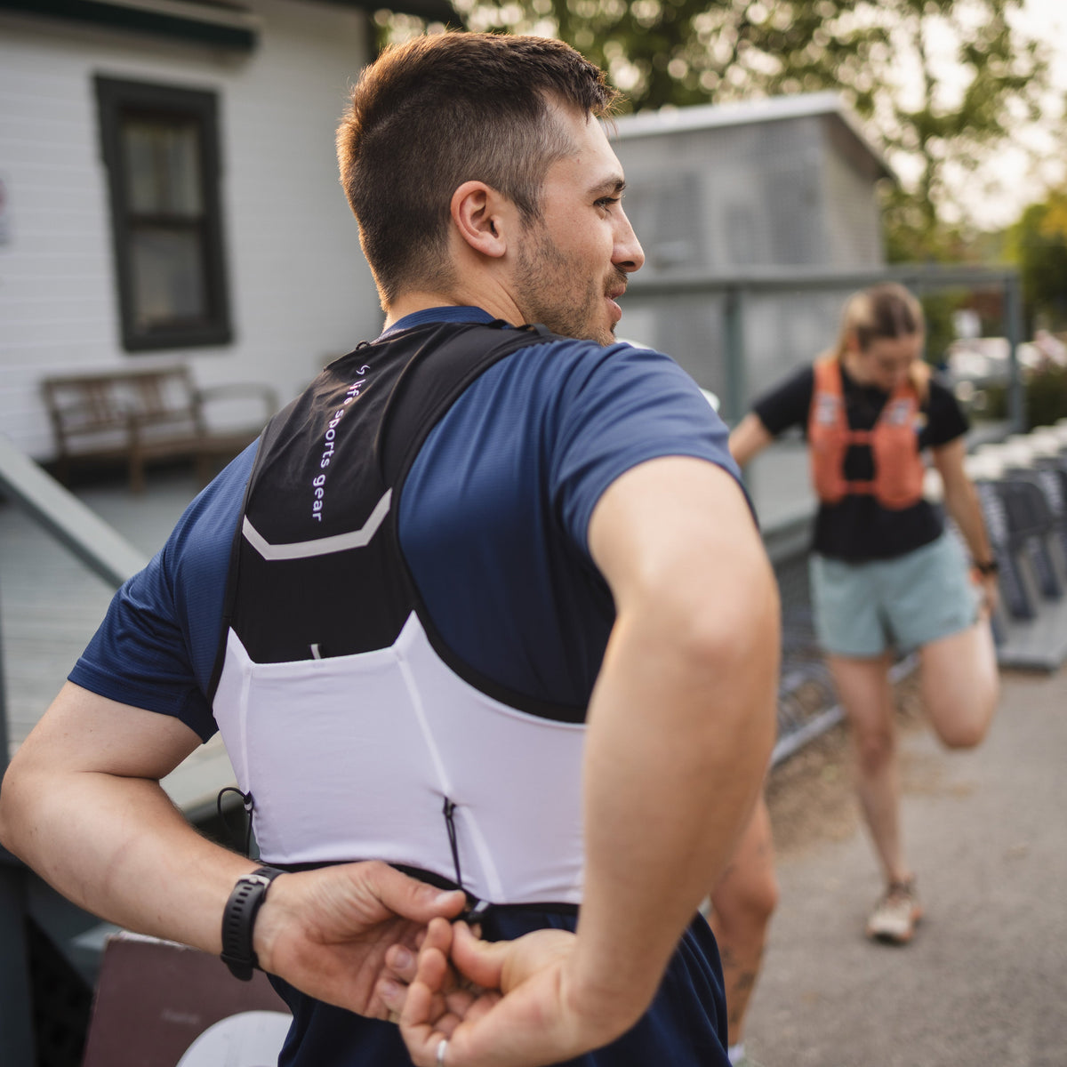 Man in athletic wear standing outdoors with another person in the background. #color_black