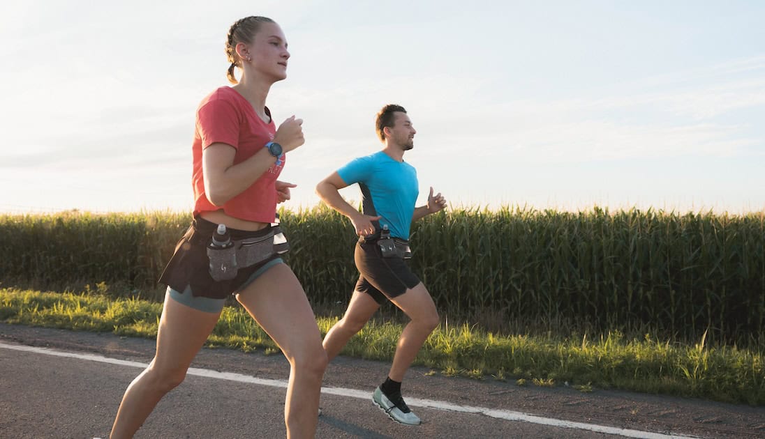 Homme et femme courant sur une route de campagne et portant une ceinture d'hydratation.