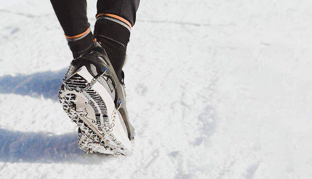 Crampons d'hiver portés sur des souliers de course par une personne pratiquant une activité sur la neige