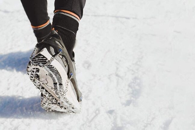 Crampons d'hiver portés sur des souliers de course par une personne pratiquant une activité sur la neige