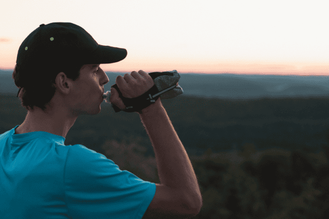 Un coureur tenant une bouteille d'hydratation compressible en regardant les montagnes au loin.