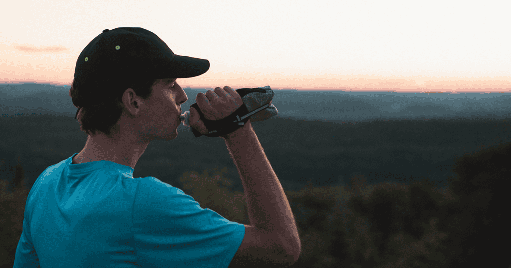 Un coureur tenant une bouteille d'hydratation compressible en regardant les montagnes au loin.