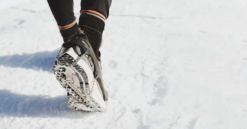 Crampons d'hiver portés sur des souliers de course par une personne pratiquant une activité sur la neige